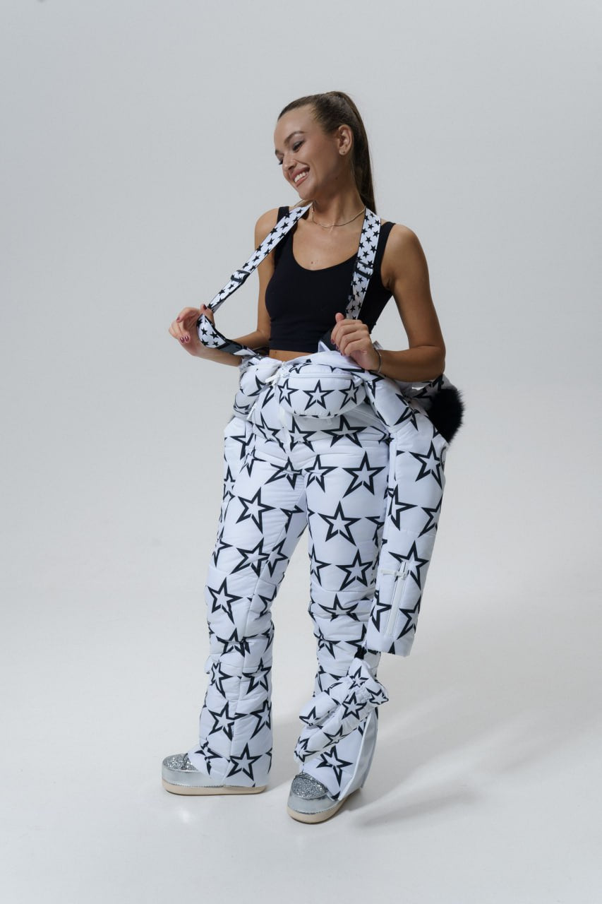 Woman wearing a black tank top and white pants with star patterns, standing against a plain background.