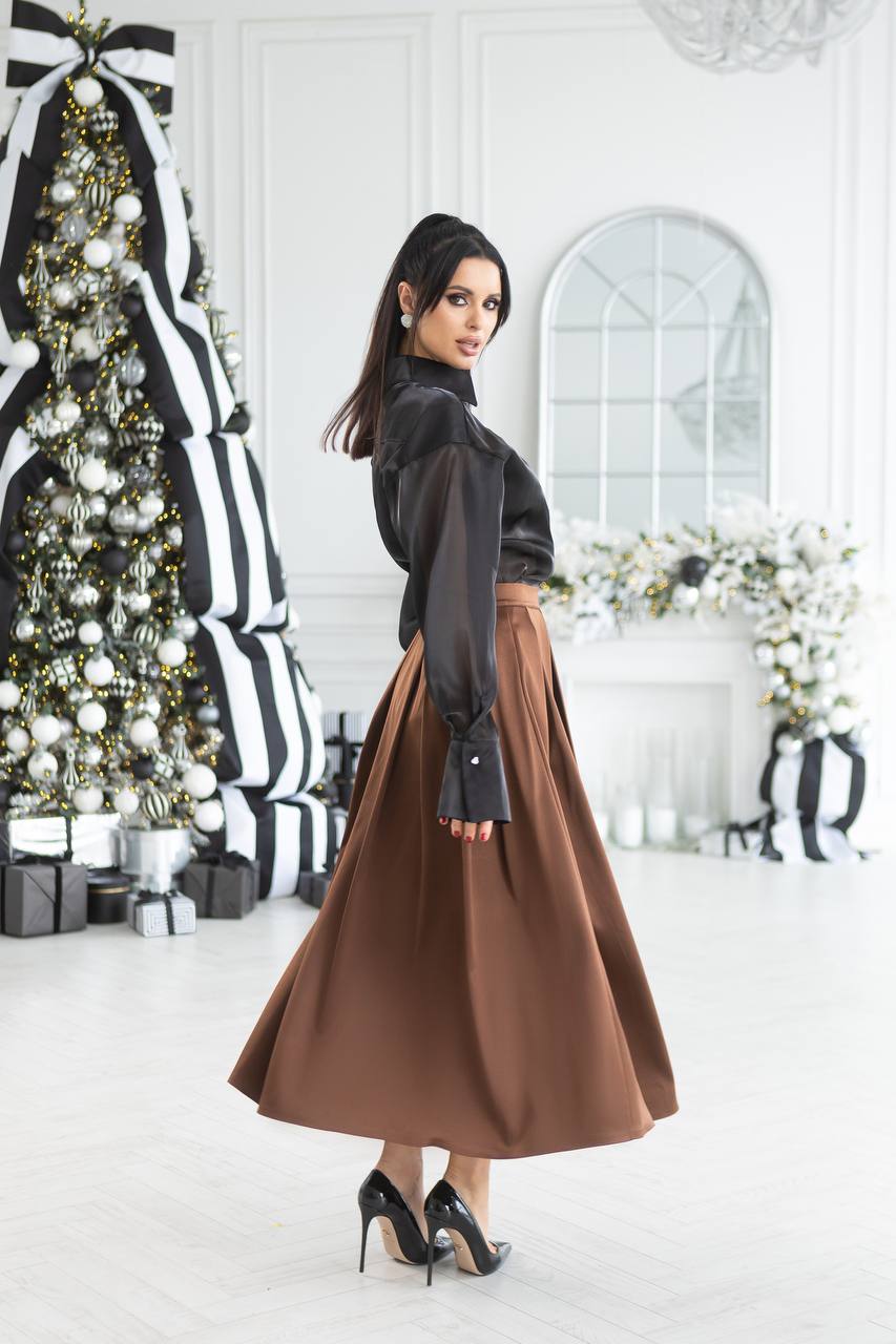 Woman in a brown skirt and black top standing in a decorated room with Christmas tree and white walls.