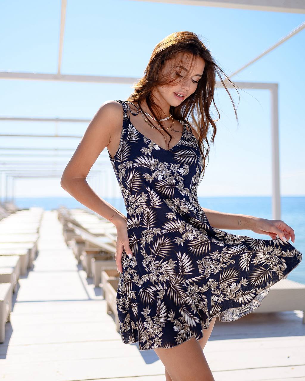 Woman wearing a navy blue dress with white floral pattern on a wooden deck by the sea.