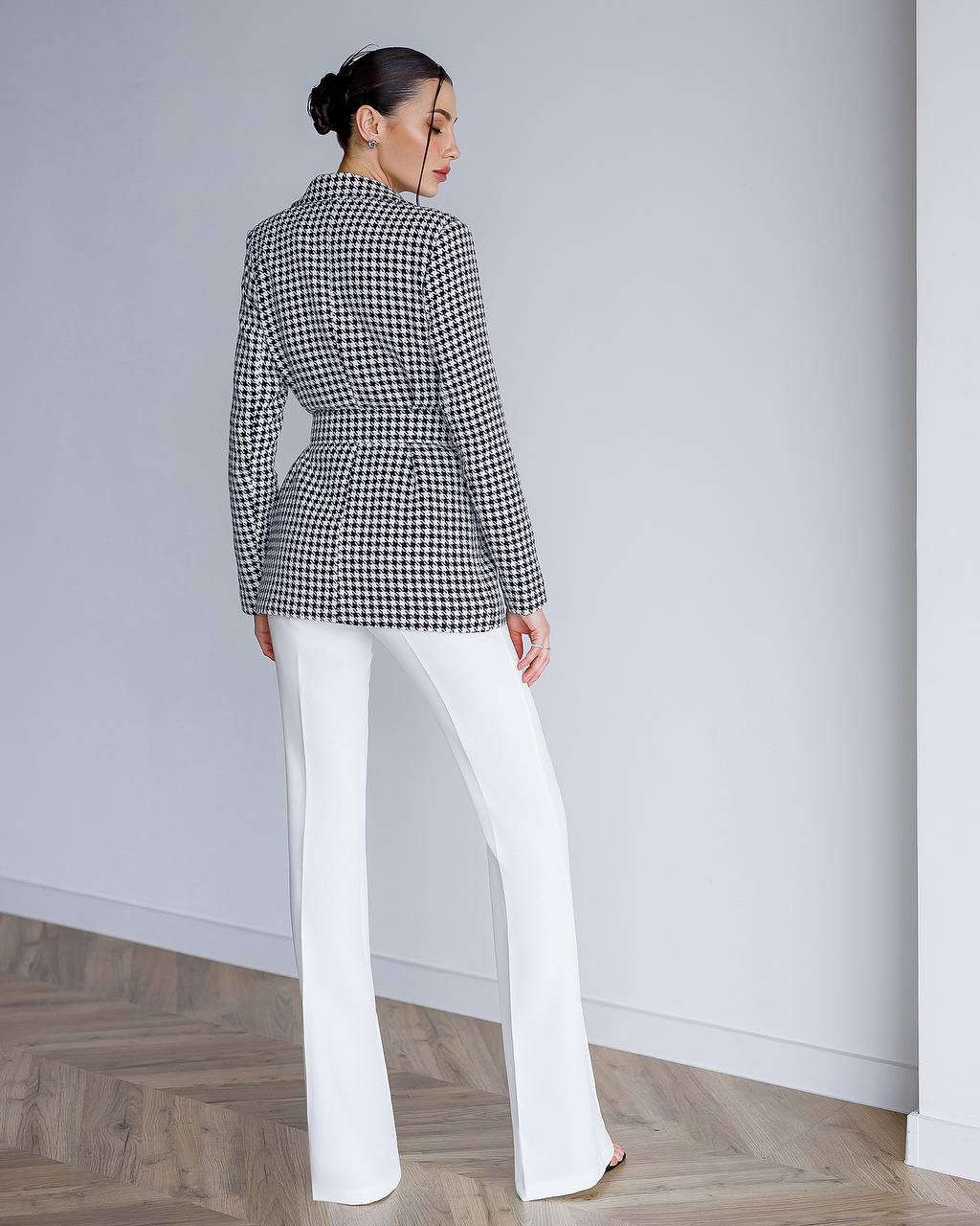 Woman wearing a black and white checkered blazer and white pants against a plain background