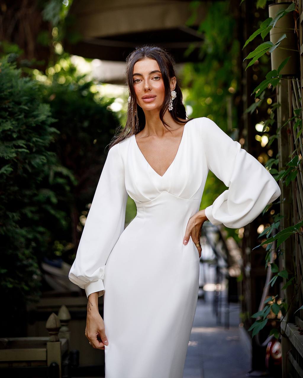Woman in a white dress standing outdoors with greenery in the background
