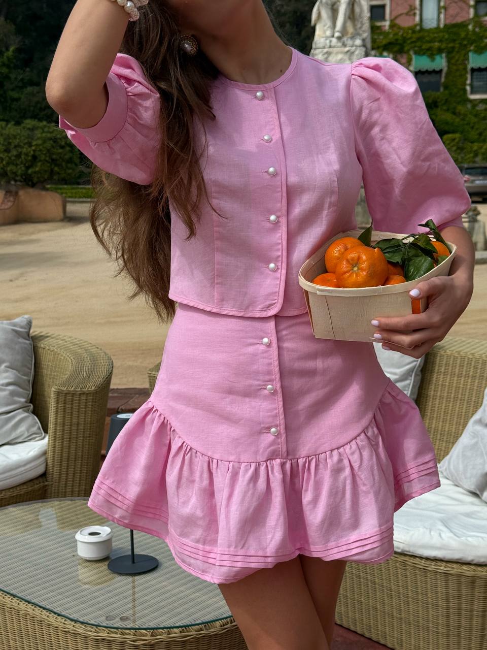 Person wearing a pink dress holding a basket of oranges outdoors.