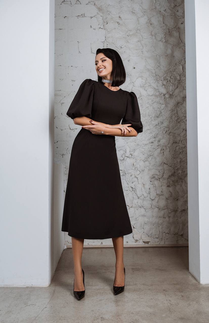 Woman wearing a black dress standing against a textured wall.