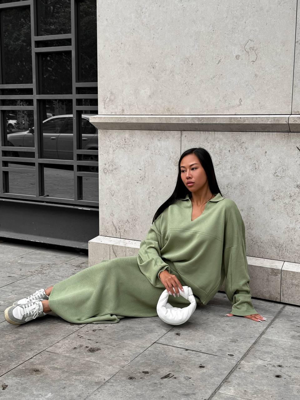 Woman in a green outfit sitting on a city street.