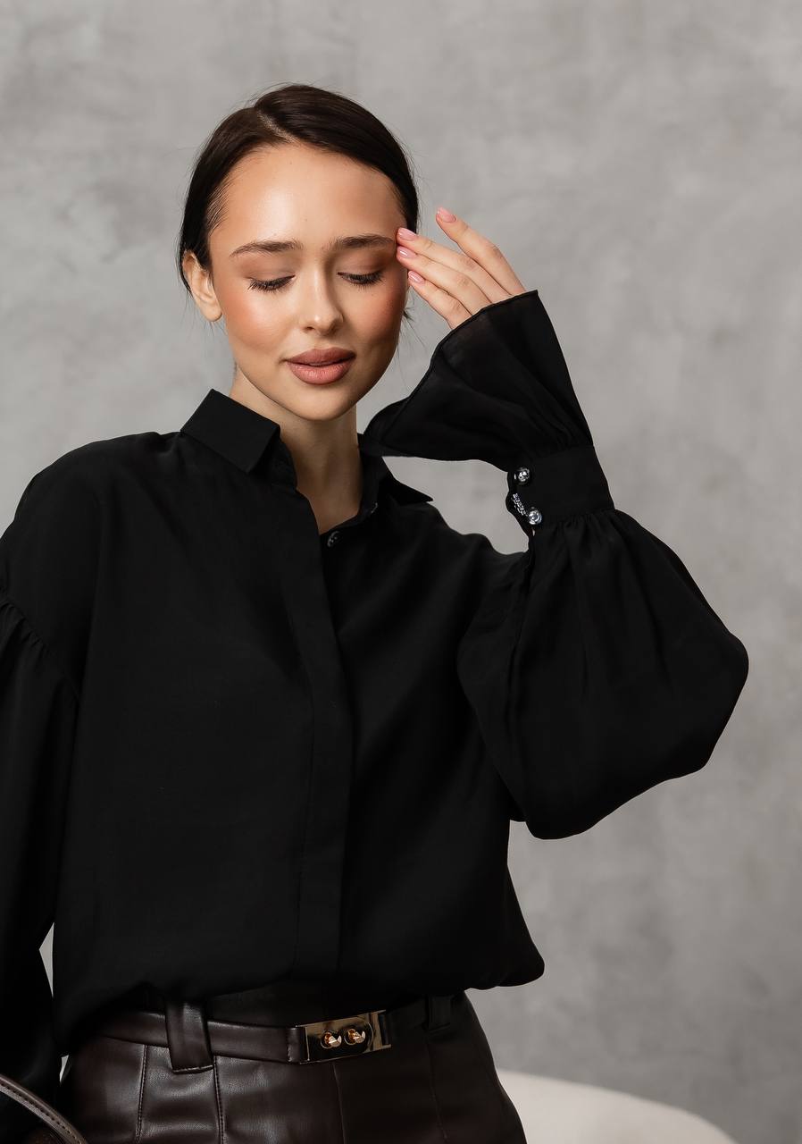 Woman wearing a black blouse with puffed sleeves against a gray background