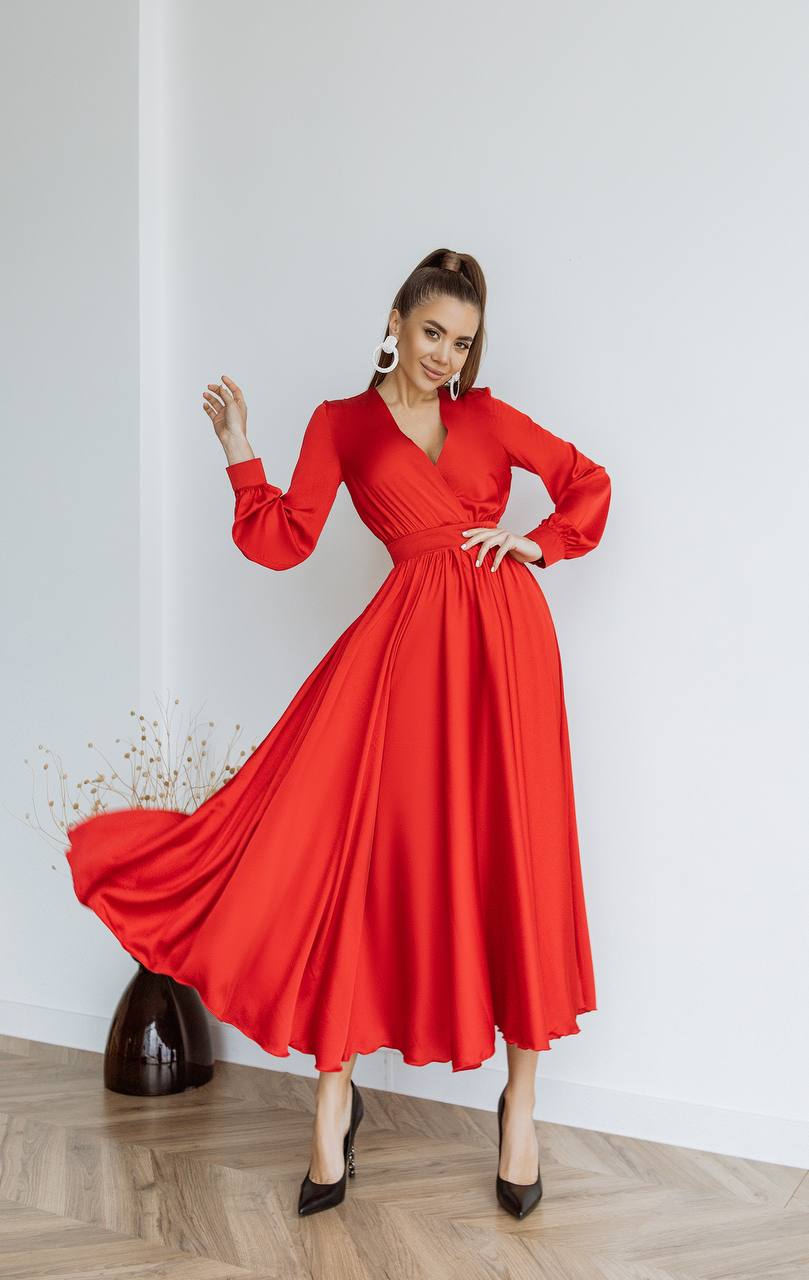 Woman wearing a red dress with long sleeves against a white wall.