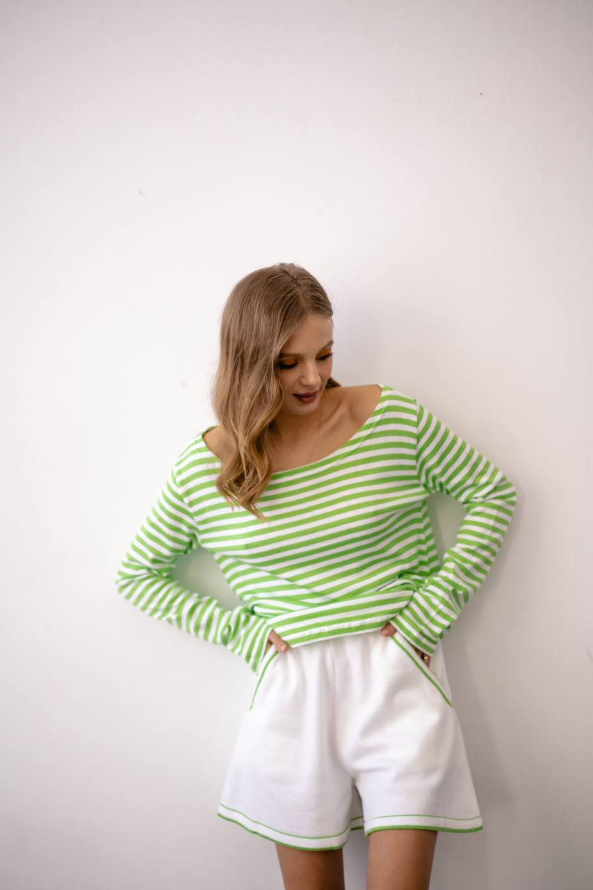 Woman wearing a green and white striped top and white shorts against a plain background