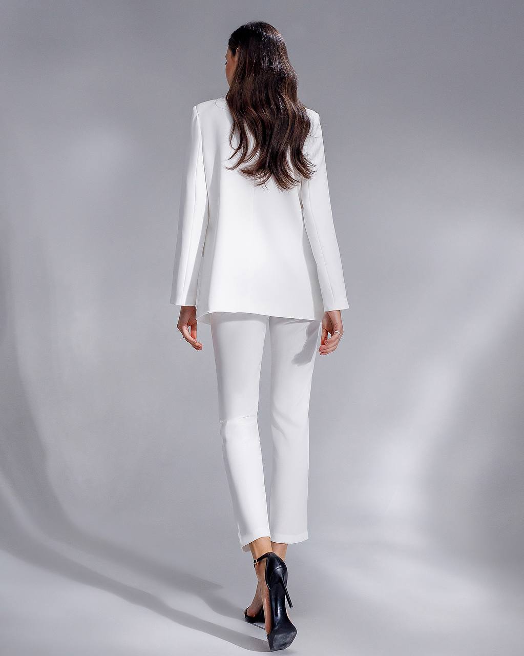 Woman wearing a white suit standing against a gray background