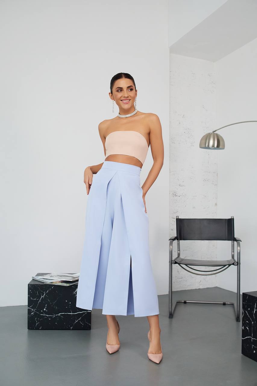 Woman wearing a beige top and light blue pants in a minimalistic room.