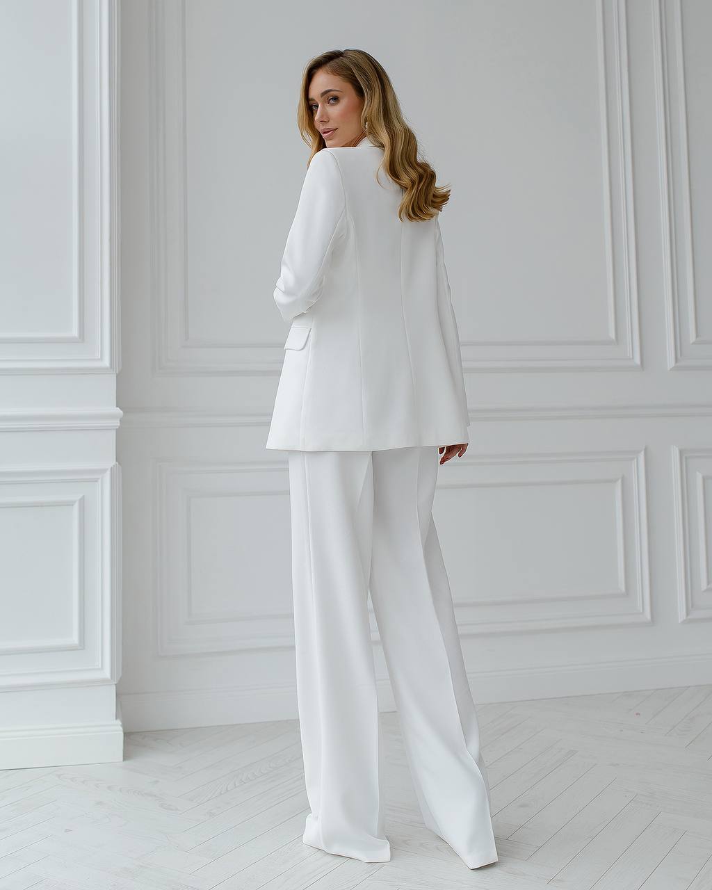 Woman wearing a white suit standing against a white wall.