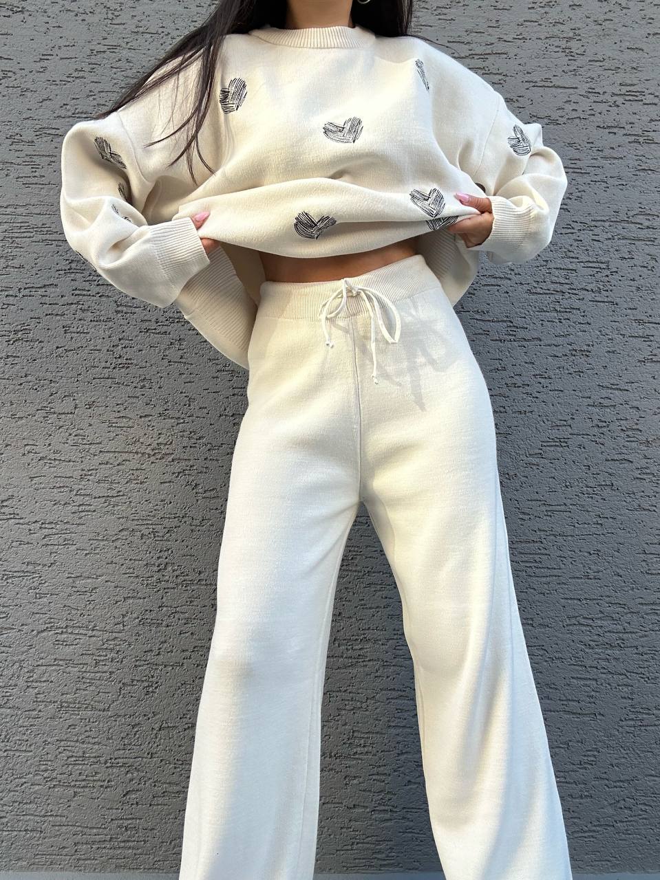 Person wearing a white outfit with embroidered designs against a gray wall.