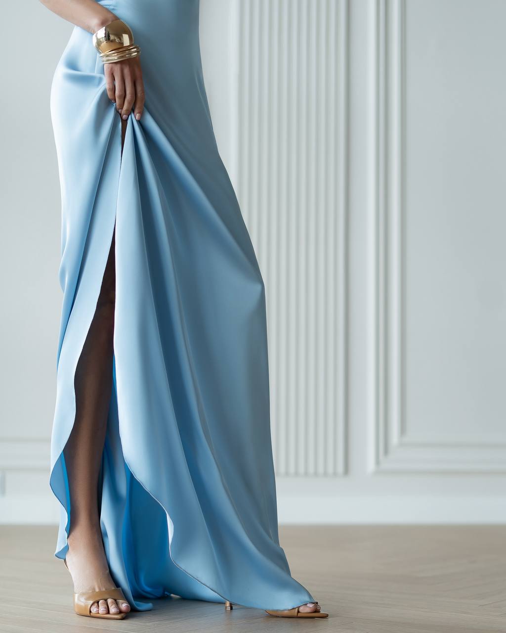 Woman wearing a light blue evening gown with a high slit in a minimalistic setting