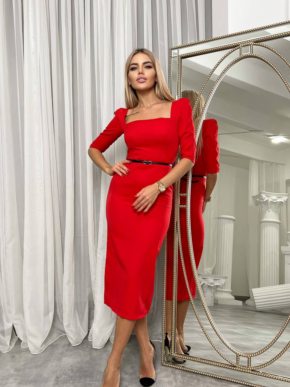 Woman in a red dress standing in front of a mirror in an elegant room.
