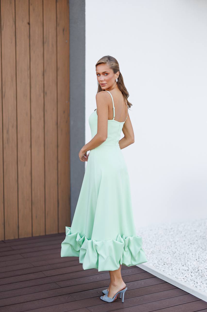 Woman wearing a light green dress with ruffled hem on a wooden deck.