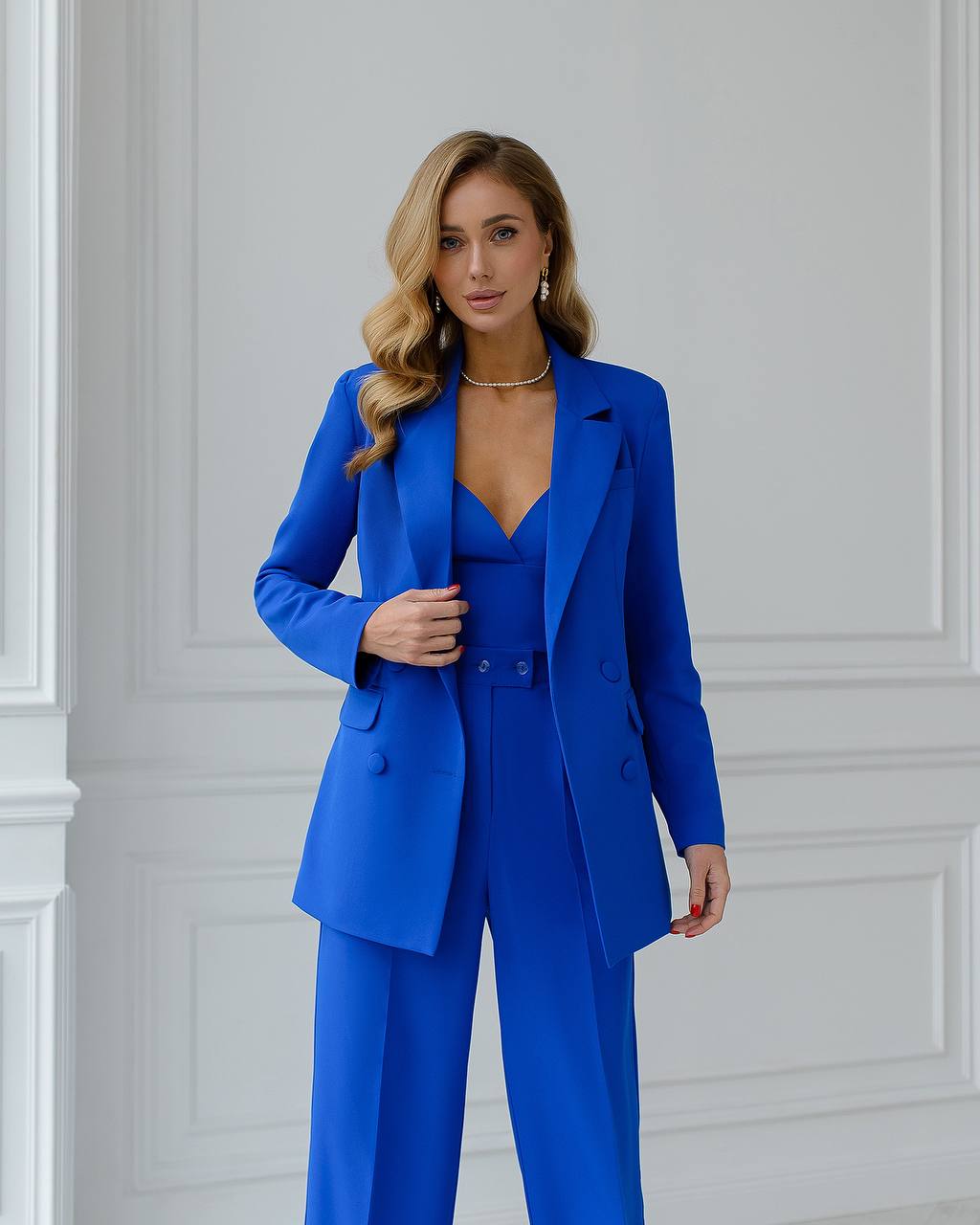Woman wearing a blue suit standing against a white paneled wall.