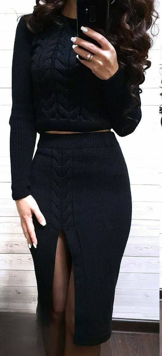 Person wearing a black cable knit top and skirt set against a white wall.