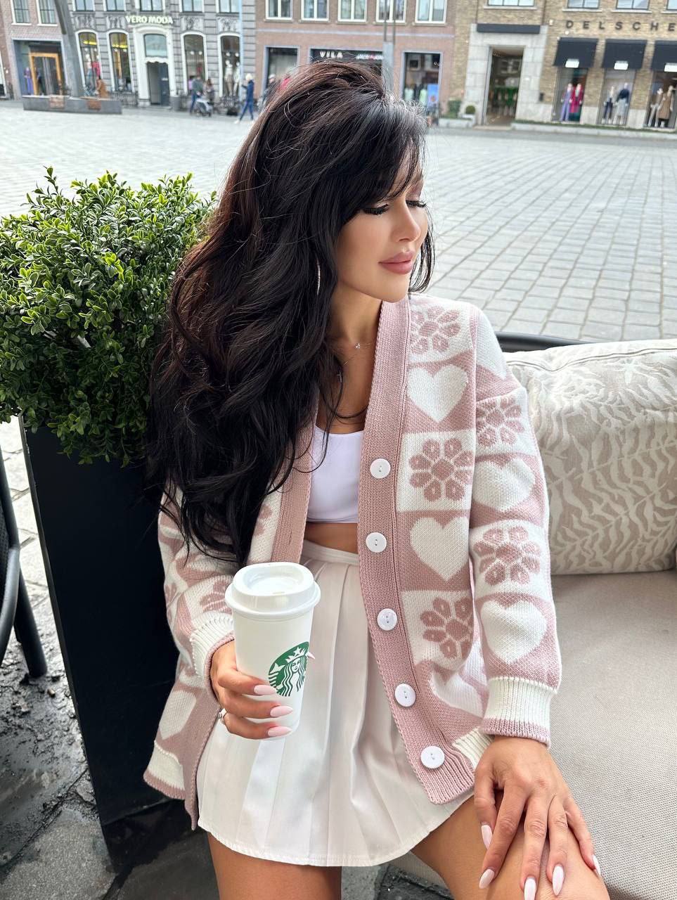 Woman holding a Starbucks cup outdoors, wearing a patterned cardigan.