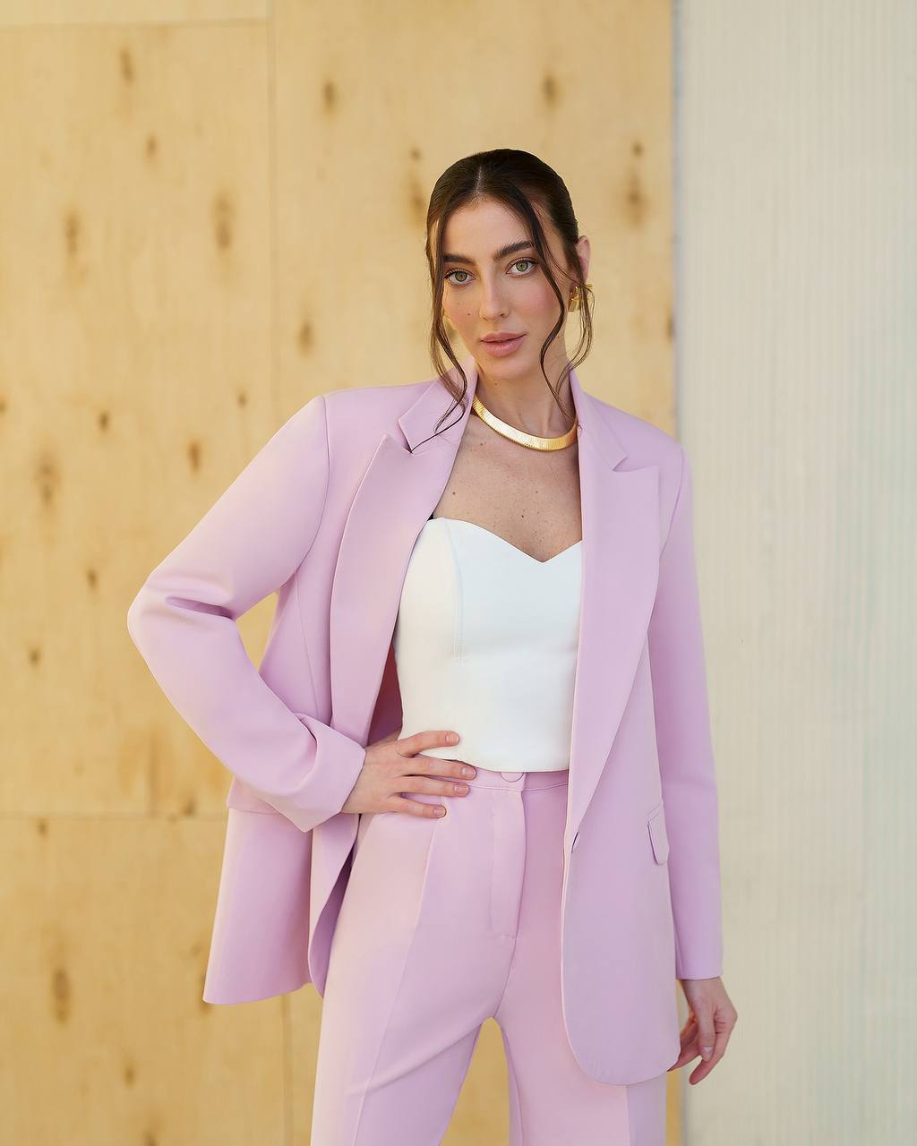 Woman wearing a light purple suit standing against a wooden wall.