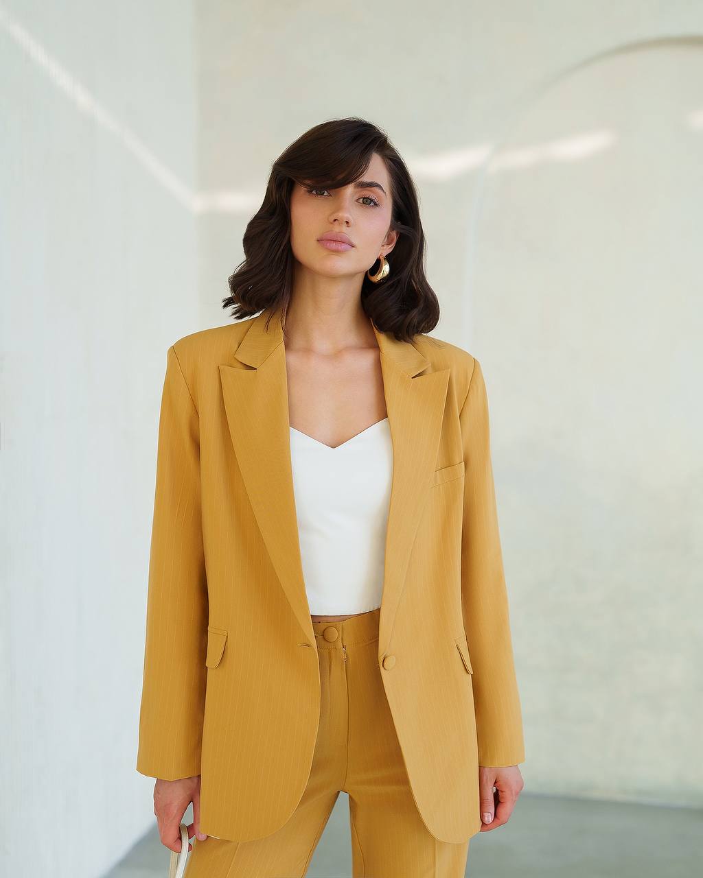 Woman wearing a mustard yellow suit against a white background