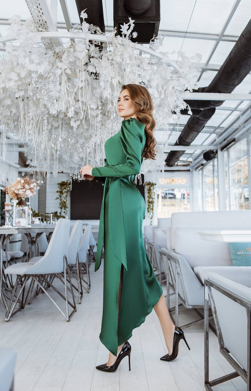 Woman in a green dress standing in a modern restaurant with white decor and chandelier.