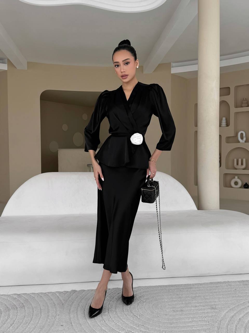 Woman in a black outfit standing in an elegant room with white furniture.
