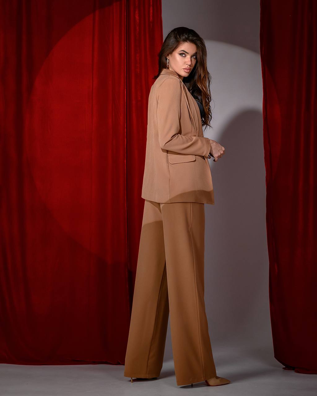 Woman in a beige suit standing against a red curtain backdrop