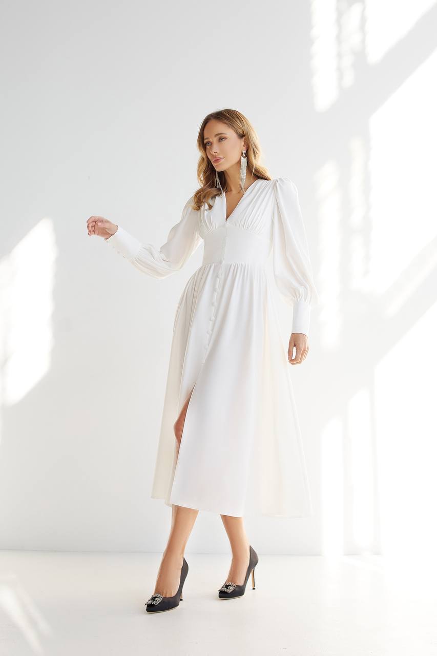 Woman wearing a white dress standing in a bright, minimalistic room.