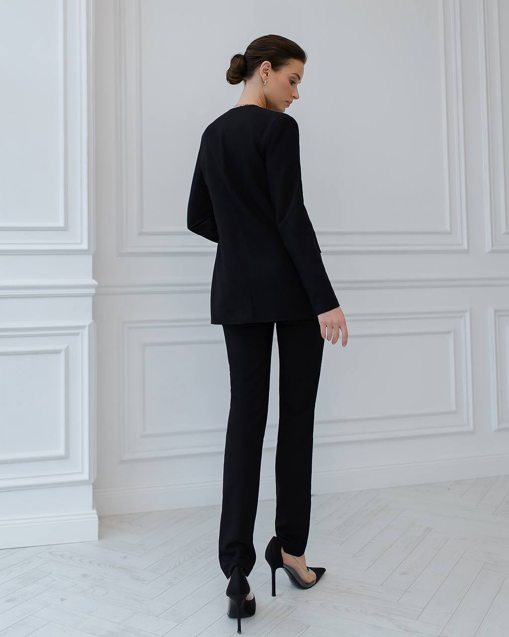 Woman wearing a black suit standing in a room with white paneled walls.