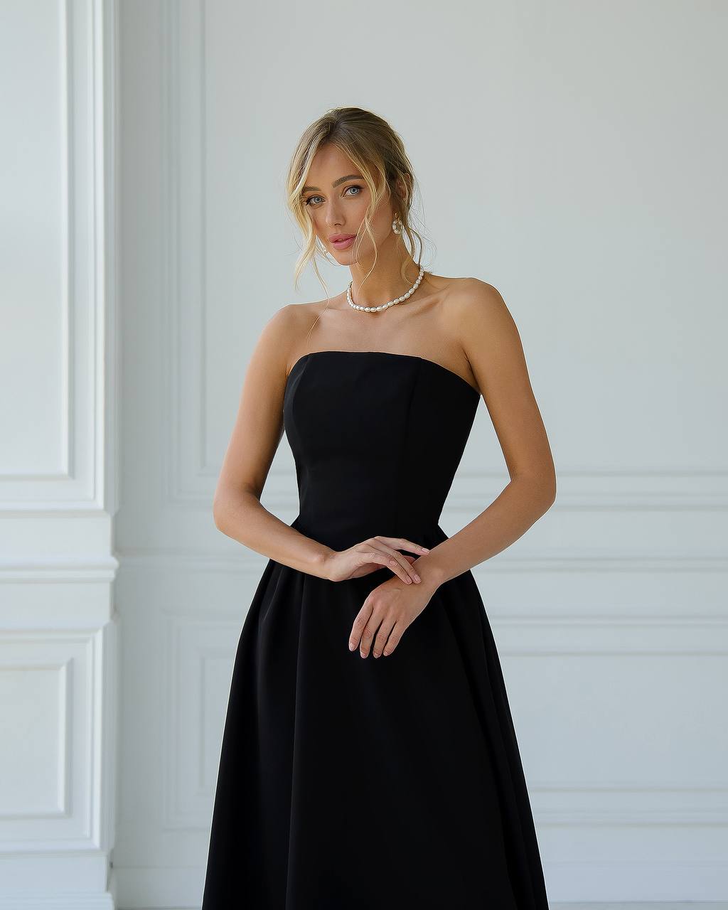 Woman wearing a black strapless dress against a white wall