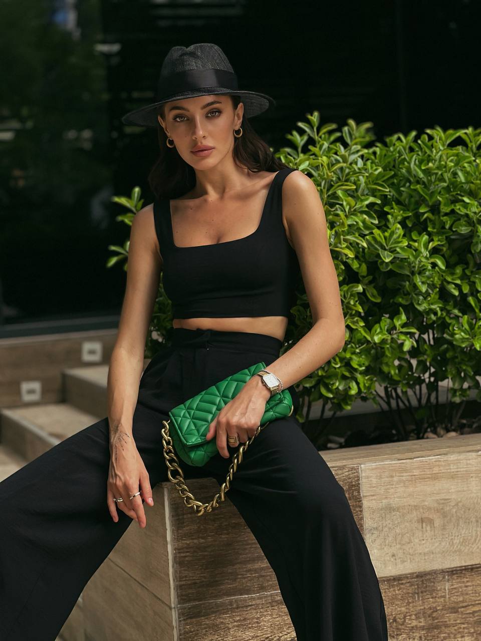 Woman in black outfit with green quilted handbag sitting on steps outdoors