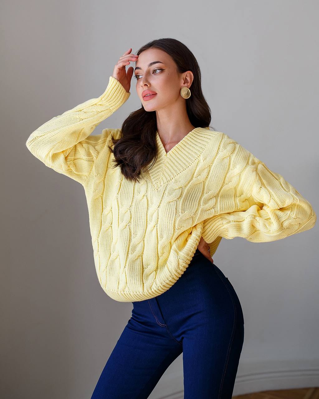 Woman wearing a yellow cable knit sweater and blue pants against a gray background