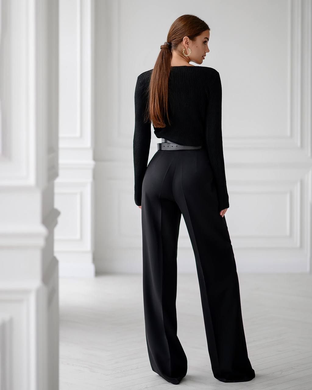 Woman wearing a black outfit with wide-leg pants in a white room.