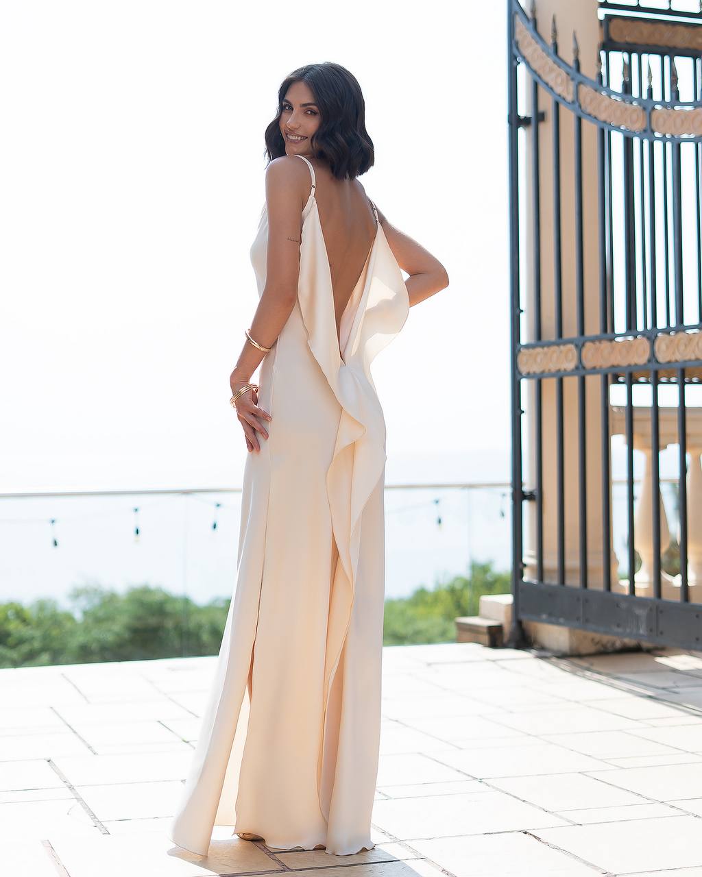 Woman in a flowing dress standing on a balcony with a scenic background