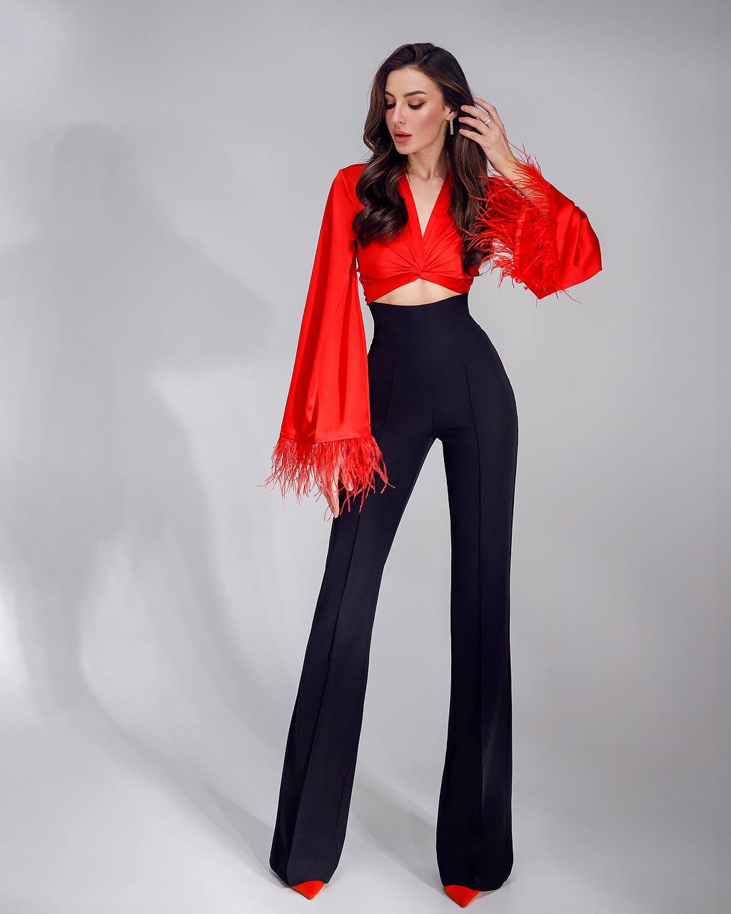 Woman wearing a red top and black pants with a red scarf on a gray background