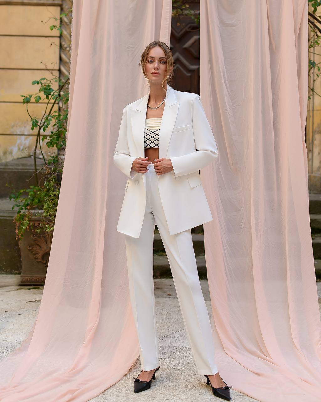 Woman in a white suit standing in front of pink curtains