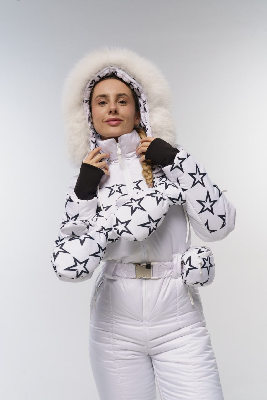 Person wearing a white snowsuit with star patterns and a fur-lined hood on a plain background