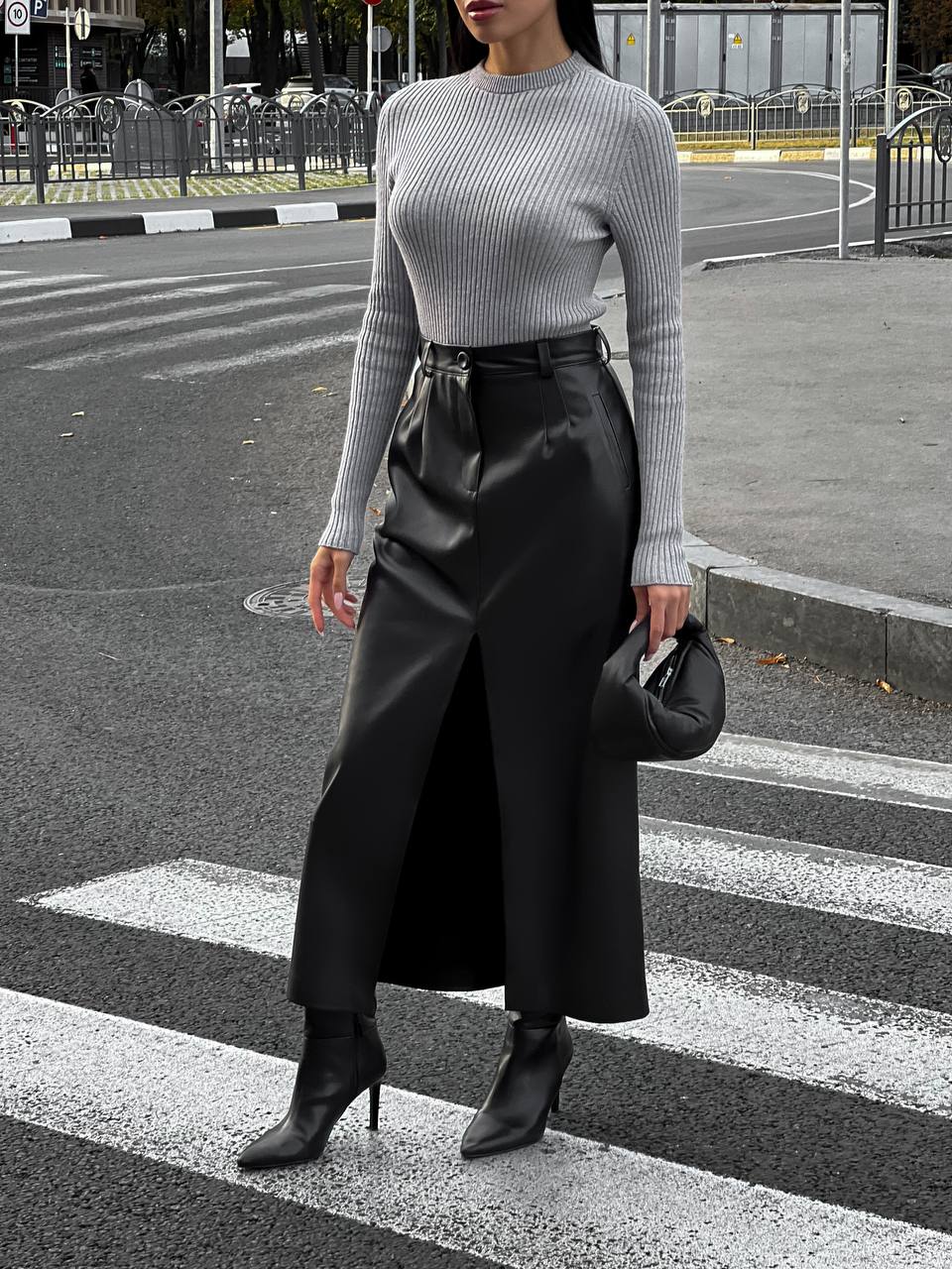 Woman in a gray sweater and black skirt crossing a street.