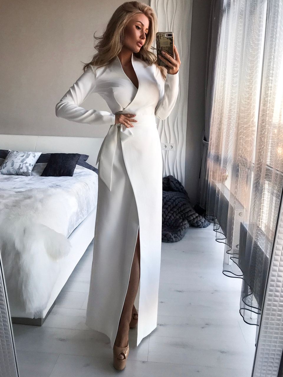 Woman taking a mirror selfie wearing a white dress in a bedroom.