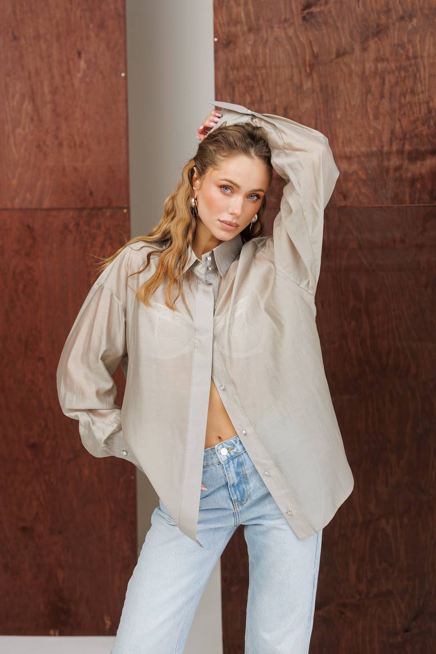 Woman wearing a beige blouse and light blue jeans against a brown wall.