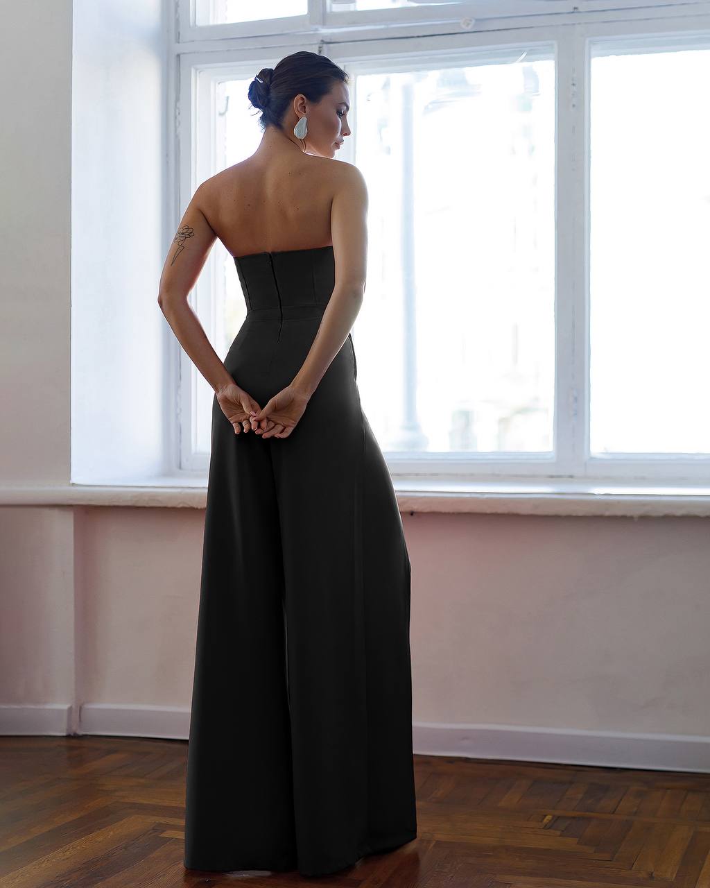 Woman in a black strapless gown standing in a room with large windows.