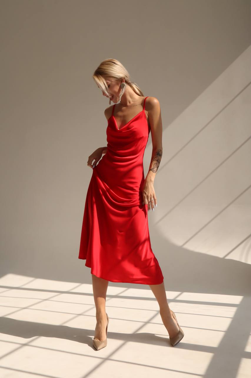 Woman in a red dress standing in a sunlit room with a neutral background