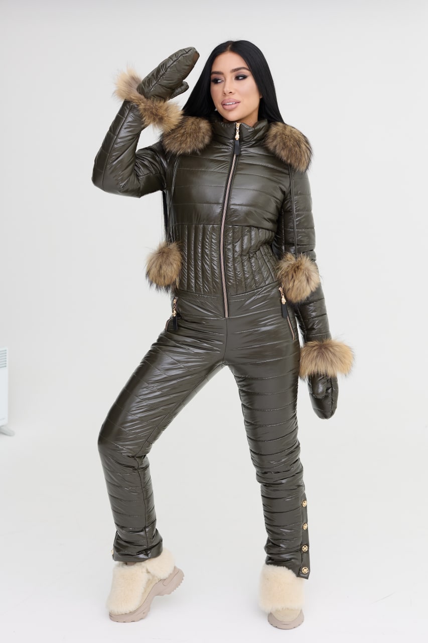 Person wearing a dark green puffer jumpsuit with fur trim on a white background