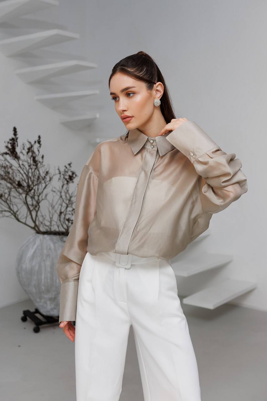 Woman wearing a beige blouse and white pants in a minimalistic setting