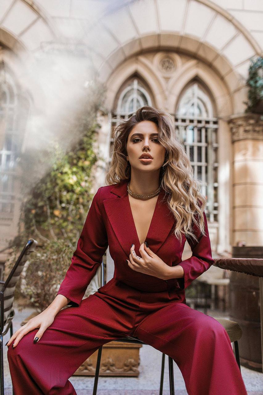 Woman in a red outfit sitting in an elegant outdoor setting with architectural elements.