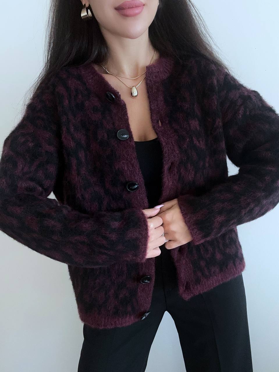 Person wearing a dark purple cardigan with a subtle pattern against a plain background