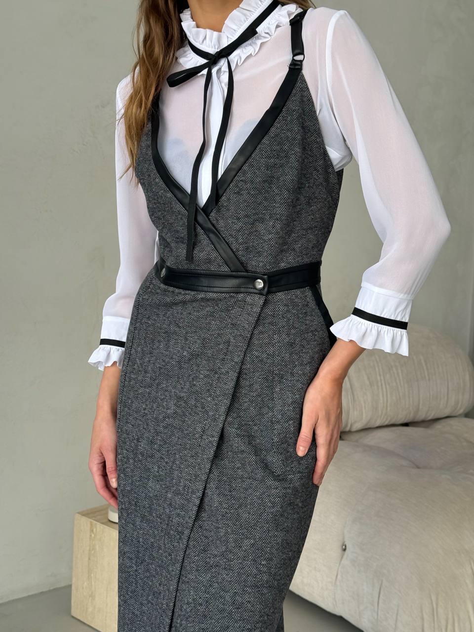 Person wearing a gray dress with a white blouse and black accents in a neutral setting.