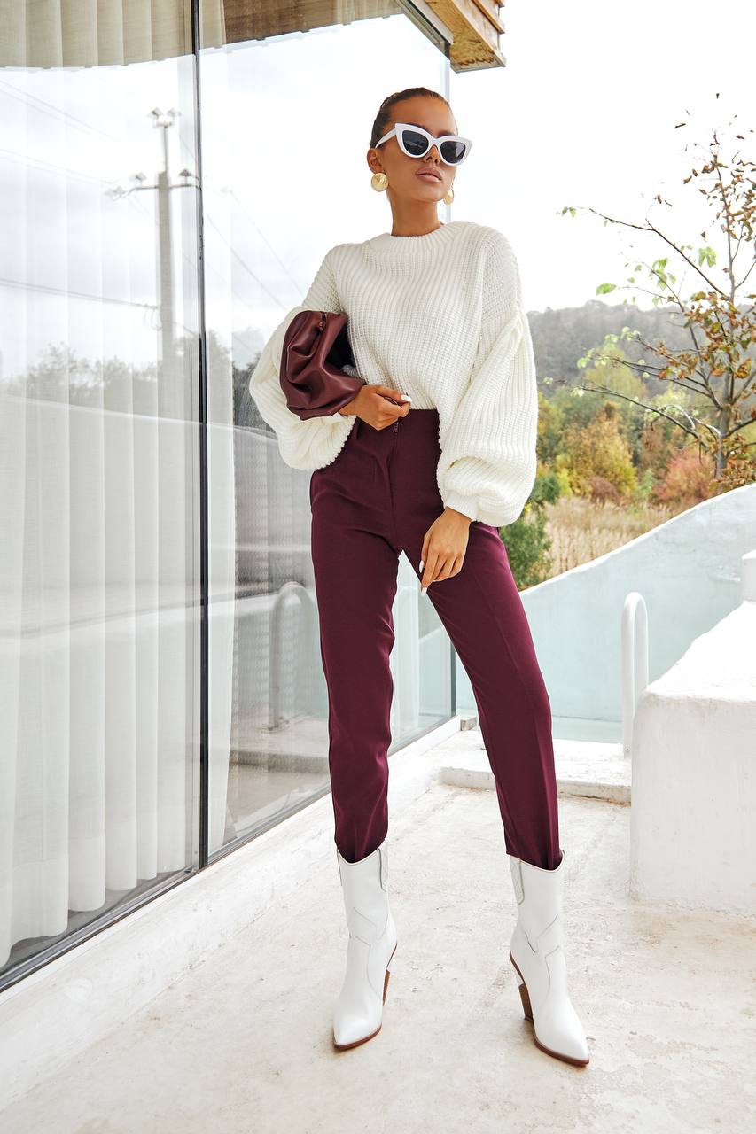 Woman in a white sweater and burgundy pants standing on a balcony.