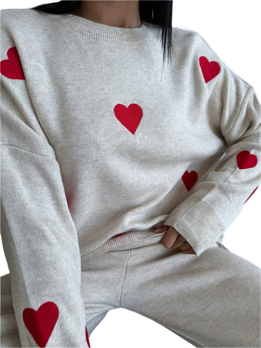 White sweater with red heart patterns worn by a person on a white background