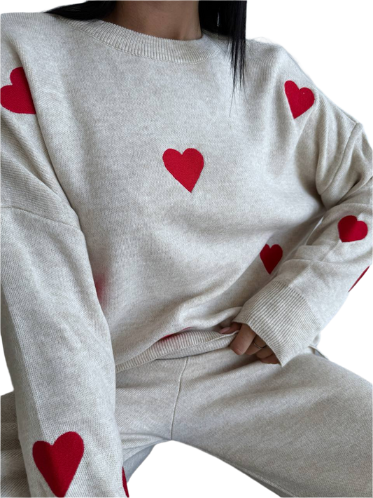 White sweater with red heart patterns worn by a person on a white background