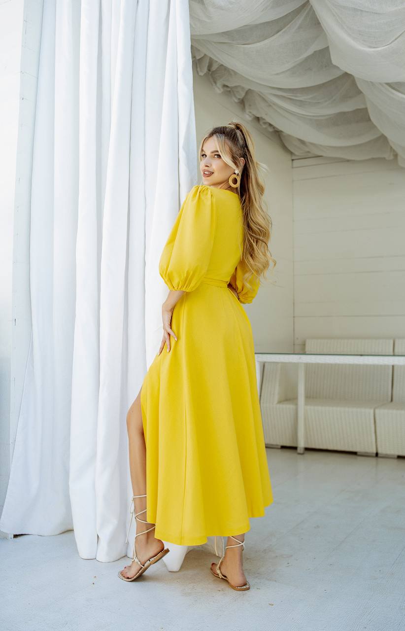 Woman in a yellow dress standing in a room with white curtains and furniture.